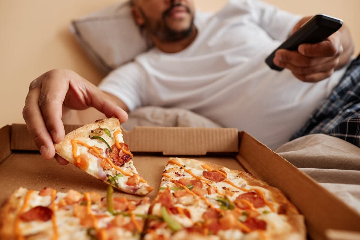 Ein Mann liegt mit Pizza vor dem Fernseher.