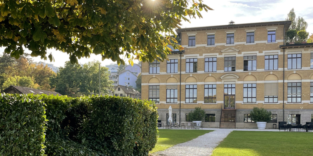 Bâtiment historique en briques jaunes avec jardin, haie et allée de gravier