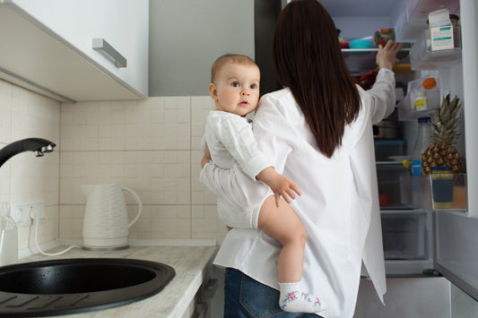 Eine Frau mit Baby auf dem Arm in der Küche.